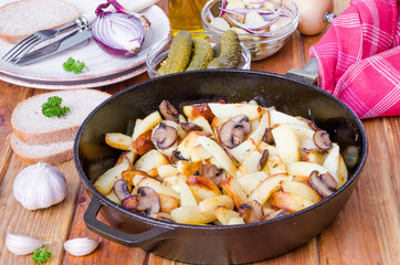 Fried potatoes with mushrooms in a pan on a wooden background