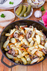 Fried potatoes with mushrooms in a pan on a wooden background