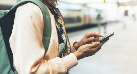 Enjoying travel. Young woman waiting on station platform with backpack on background electric train using smartphone. Tourist texting message and plan route of railway, railroad transport concept