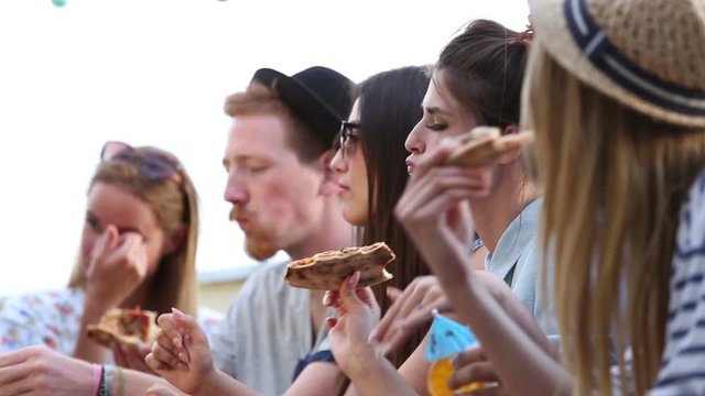 Group of young friends enjoying at a party while eating pizza