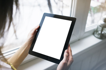 Hipster person hands holding digital tablet with empty blank screen, against a background of  window horizontal,  freelancer girl using at home on a computer on the balcony, mockup teghnology,  blur