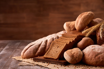 Freshly baked bread loaves on burlap on wooden table with brown blurred background. Texture closeup bakery products