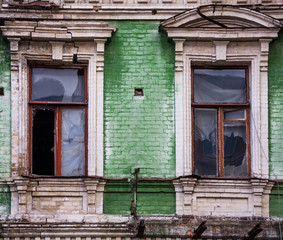 Fototapeta na wymiar Two broken wooden windows on green brick facade of an old unkempt and vandalized house in Kiev (Kyiv), the capital of Ukraine