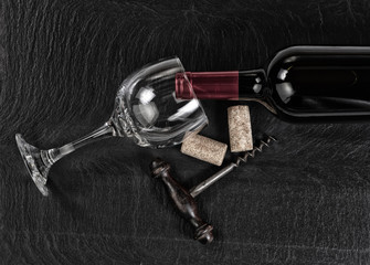 Overhead view of vintage corkscrew with red wine bottle and glass on black slate background