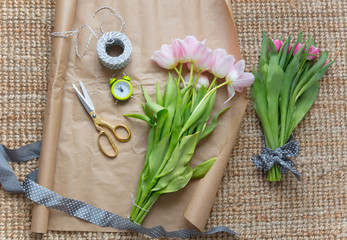 photo of beautiful pink bunches of pink tulips, alarm clock and things for wrapping on the wonderful carpet background