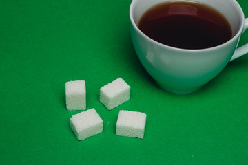 cup with a drink and cubes of sugar on a green background