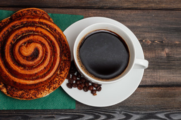 a cup of coffee on a saucer and a cinnamon roll on a green napkin
