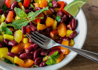 Close-up on red kidney beans and peppers salad on serving plate, a fork and a slice of lime, ready...
