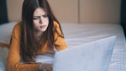 woman working behind laptop lying on bed