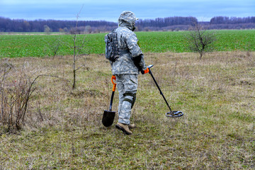 Man with a device for finding treasures with a shovel on the field