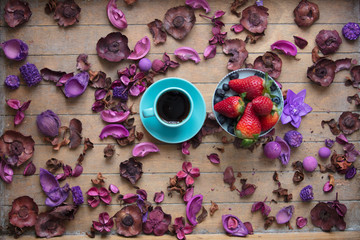 photo of cup of coffee and fresh blueberries and strawberries near wonderful dried flowers petals on the wooden background