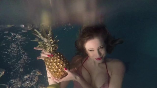 Slender girl in a swimsuit with pineapple in a pool under water. Underwater shooting