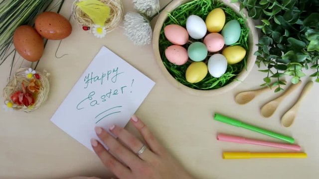 Hand with marker doing postcard and Easter decorations on wooden background