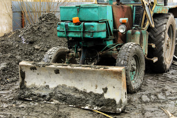 An old Soviet tractor digs and loads waste stone processing near the shop