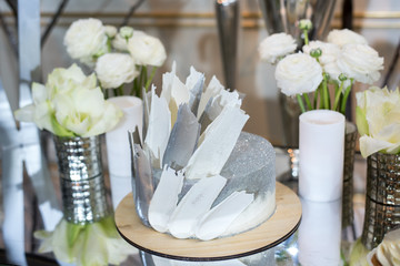 Wedding cake in silver color with glitters on the table decorated with flowers and candles
