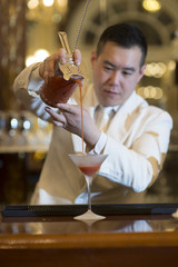 Chinese Barman is making cocktail at night club.