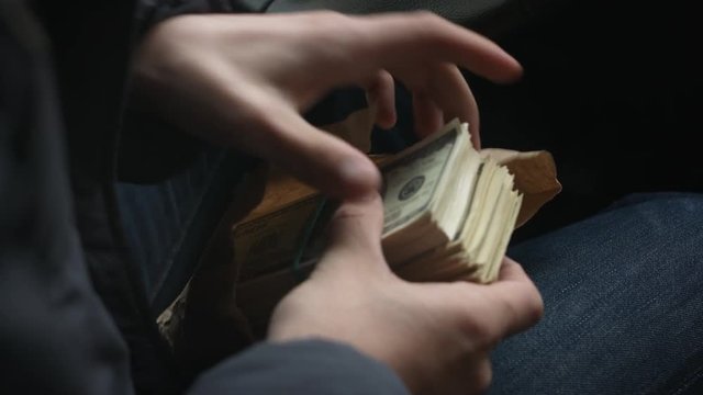 View from over shoulder of man pulls from the package large sum of money sitting behind the wheel of car, close up shots