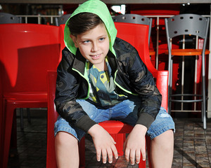 casual child sitting on a red chair in the bar wearing a colorful knitted green and jeans