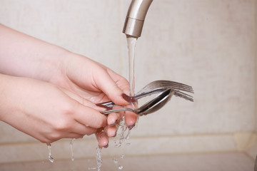 Hands of a close-up girl. girl washes forks and spoons under stream of water