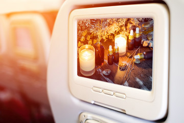 Aircraft monitor in front of passenger seat showing bottles with organic essential aroma oil with dry flower on old wooden background.