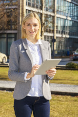 Junge Business-Frau draußen in der Mitagspause mit Tablet in der Hand und lächelt in die Kamera