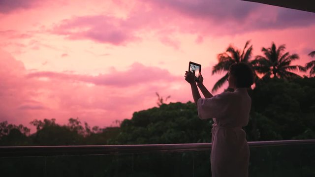 Young woman taking pictures of sunset above the rain forest using tablet computer.