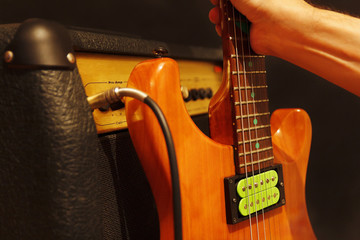 Fototapeta premium Hand puts electric guitar to amplifier on the black background. Shallow depth of field, low key, close up.