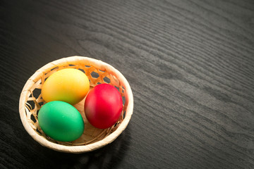 Multicolored easter eggs in a basket on a textured black wooden background. The concept of a holiday and a happy Easter. With space for text