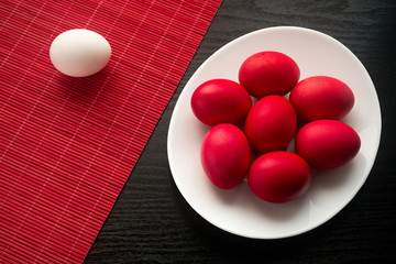 Red and white easter eggs on a red bamboo napkin with a white plate on a textured black wooden background. The concept of a holiday and a happy Easter. With space for text