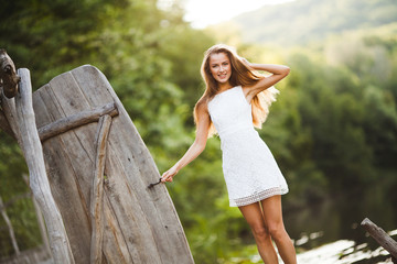 Charming long-haired smiling happy brunette girl attractive model in a white dress walk by the river.