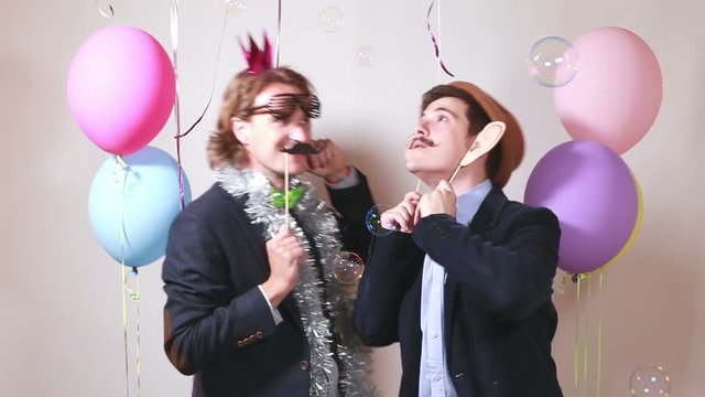 Two funny male friends dancing with props in photo booth