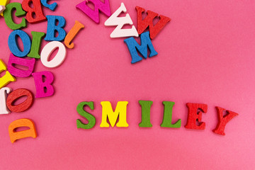 Scattered multicolored letters on a pink background, the word "smiley".
