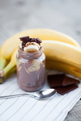 Chocolate pudding with banana in a glass jar on a textile background