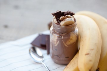 Chocolate pudding with banana in a glass jar on a textile background