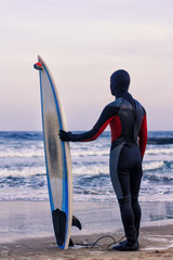 Surfer with surfboard standing on sand . He wears  a wetsuit