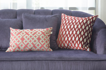 Red pattern pillows lay on vilolet sofa in living room