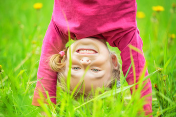 Happy little girl standing upside down on green grass in summer park