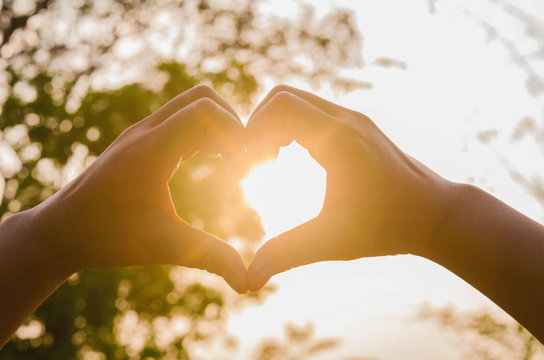 hands in shape of love heart and sunshine