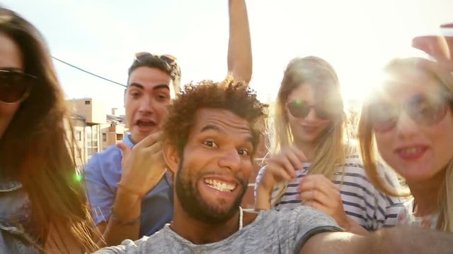 Close up of happy crazy multi-ethnic group of friends filming themselves at rooftop party on sunny day, graded