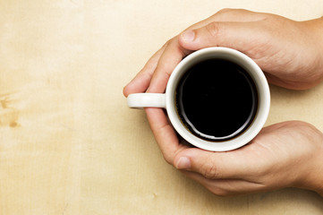 A female holding a cup of coffee on wooden table background.