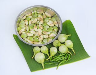 Sliced fresh organic eggplant in water and green chilli on banana leaf against white background