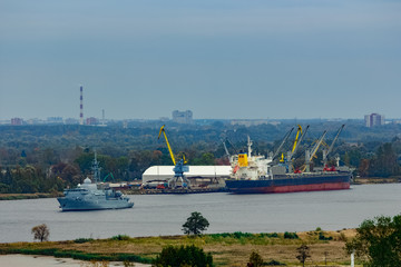 Military ship sailing past the cargo port in Riga, Latvia