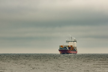 Red cargo container ship sailing from Baltic sea in cloudy day