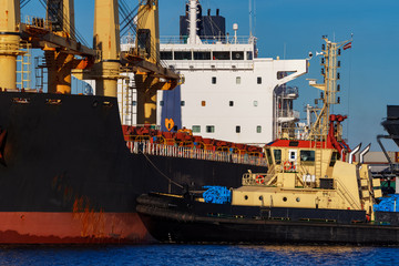 Black cargo ship mooring at the port with tug ship support
