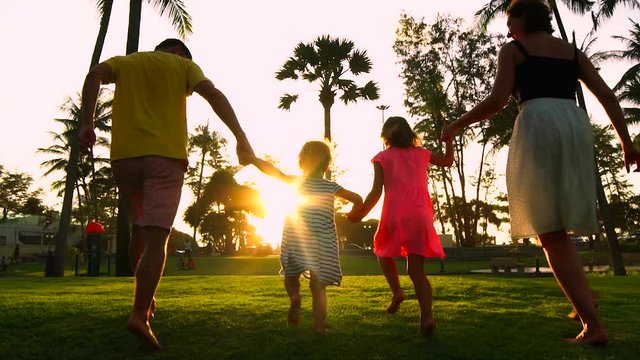 Happy family with two little daughters having fun running at sunset. Slow motion.