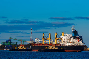 Fototapeta premium Black cargo ship mooring at the port with tug ship support