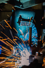 Worker is welding automotive part in car factory
