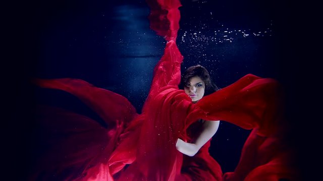 Delightful young girl athlete shows show under water dance with long red dress