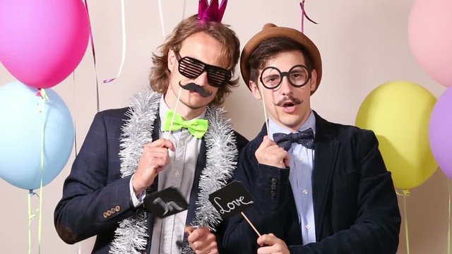 Two cheerful guys holding sign in love in photo booth