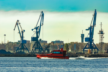 Fototapeta premium Red pilot ship moving past the cargo cranes